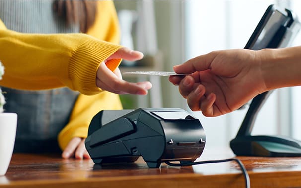 A person hands their debit card to a sales person at a counter. They are near a payment system