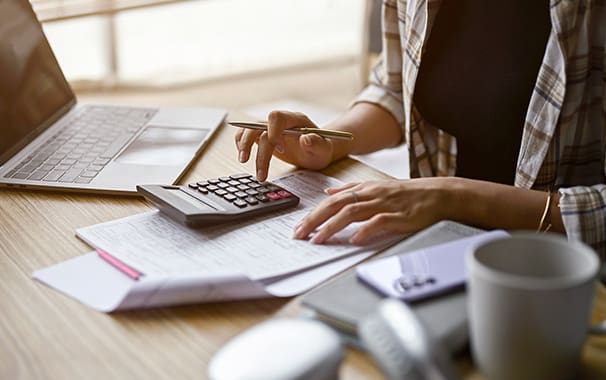 A photo of a person sitting at a desk, typing into a calculator. The photo is focused on the person's hands.
