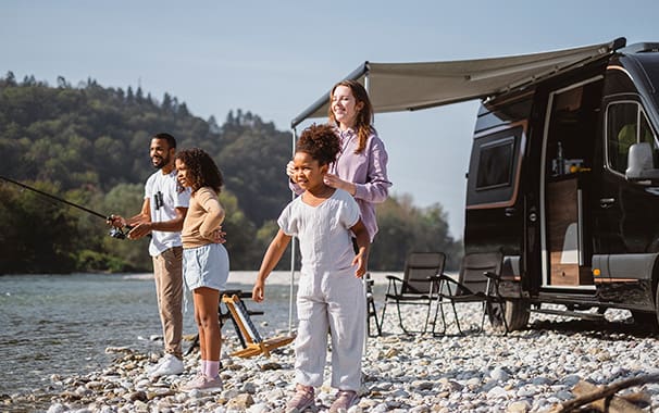 Four people are outside at their campsite with an RV in the background