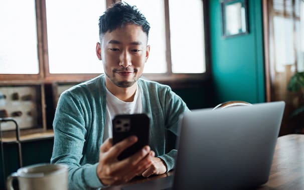 A man is seated on a sofa and holding his phone in his hands, and he is looking at the screen